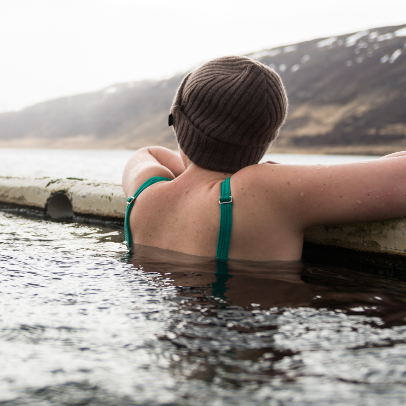Woman sits in hot spring overlooking misty mountains