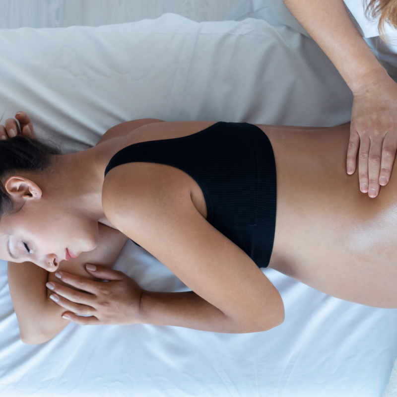 Pregnant person lies on massage table. Massage therapist massages their belly.